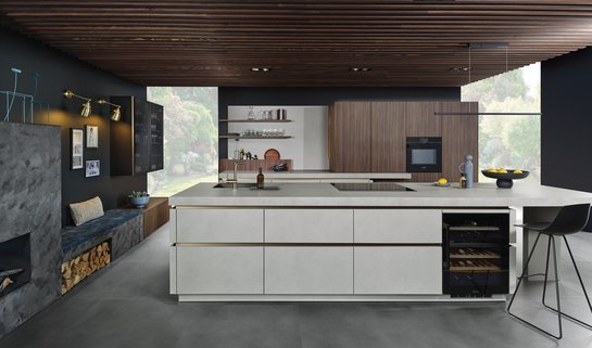 Kücheninsel mit grauer Strukturoberfläche und eingebautem Weinkühlschrank, dahinter Hochschränke in Nuss-Optik