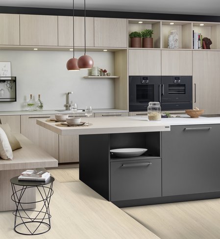 Inselküche mit dunkler Kücheninsel mit Sitzplatz vor einer Küchenzeile aus hellem Eichenholz