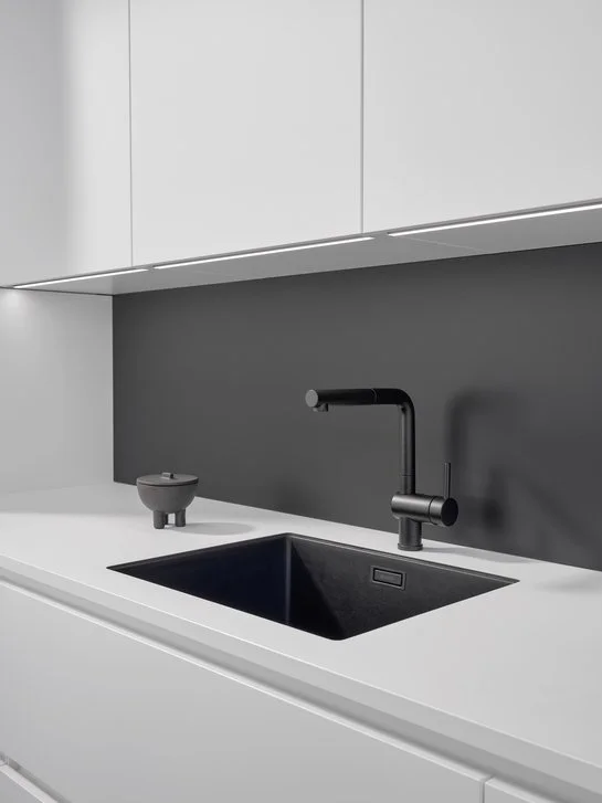 Ausschnitt einer weißen Küchenzeile mit dunkelgrauer Rückwand und schwarzer Spüle