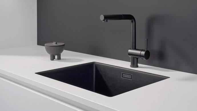 Ausschnitt einer weißen Küchenzeile mit dunkelgrauer Rückwand und schwarzer Spüle