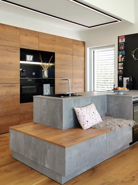 Inselküche mit Kücheninsel in Betonoptik mit integrierter Sitzbank, dahinter Hochschränke in Holzoptik