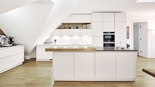 Weiße matte Küche mit Kücheninsel, die perfekt an eine Dachschräge angepasst wurde