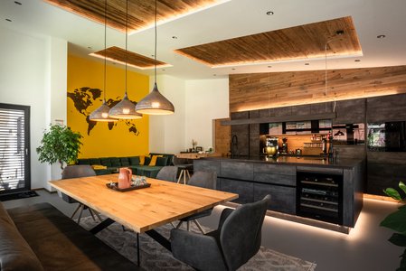 ewe Concreto in beton schiefergrau | Schuler - der Tiroler Wohnsinn Inselküche in dunkler Betonoptik mit Holzumrahmung, davor eine Essplatzgruppe