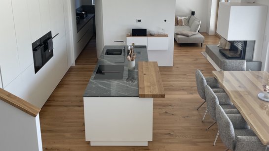 Blick von oben auf eine weiße Inselküche und einen Esstisch