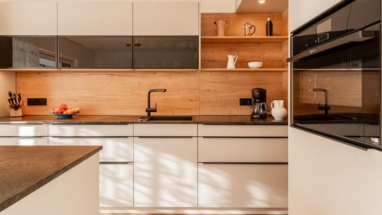 Helle Küchenzeile mit Rückwand in Holzoptik und schwarzer Arbeitsplatte