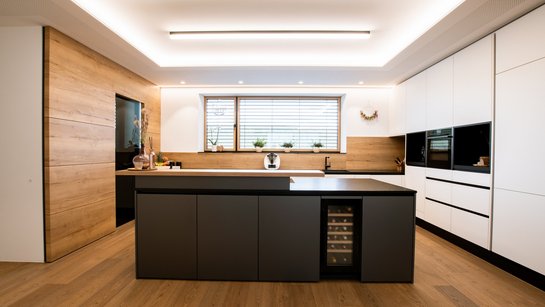 Küche mit weißer Küchenzeile rechts und einer dunkelgrauen Kücheninsel mit Weinkühlschrank integriert