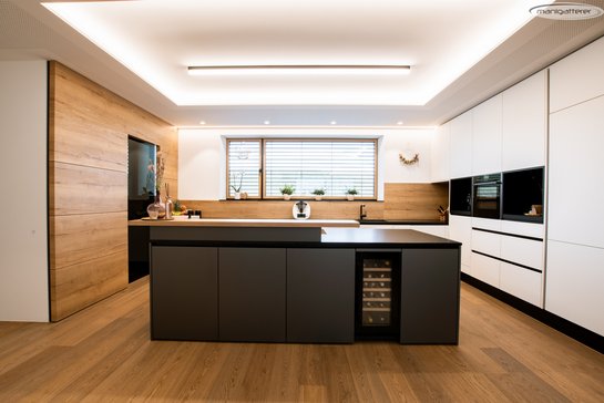 Küche mit weißer Küchenzeile rechts und einer dunkelgrauen Kücheninsel mit Weinkühlschrank integriert