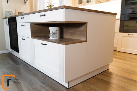 Detailbild einer Kücheninsel in weißen Rahmenfronten mit holzverkleideter Nische