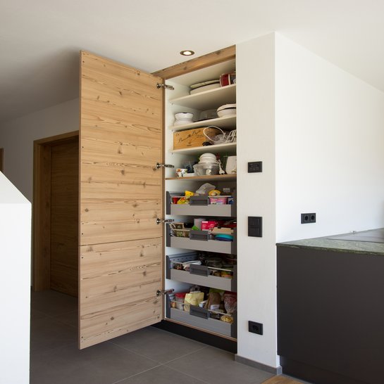 Geöffnete Holztür, dahinter ein Vorratsschrank mit Schubladen, der in die Wand eingebaut wurde
