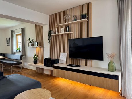 Gesamtansicht des Wohnzimmers mit TV-Wand und Lichtelementen, harmonisch abgestimmt auf Boden und Vorhänge.