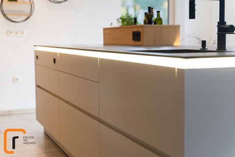 Weiße Kücheninsel mit schwarzer Dünnarbeitsplatte, die darunter beleuchtet ist.