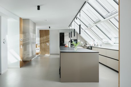 Seitliche Ansicht einer hellen Inselküche mit schwarzen Griffmulden unter schräger Fensterfront