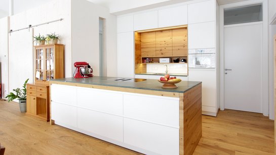 Weiße Inselküche mit warmen Holzelementen und dunkelgrüner Steinarbeitsplatte