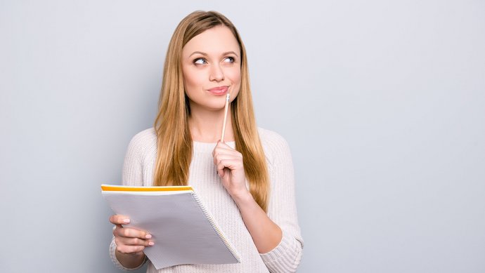 Die neue Küche will gut durchdacht sein! Eine junge blonde Frau hat einen Block und einen Stift in der Hand und überlegt intensiv.