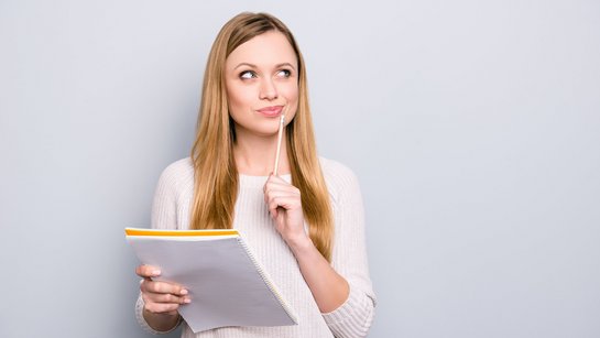 Die neue Küche will gut durchdacht sein! Eine junge blonde Frau hat einen Block und einen Stift in der Hand und überlegt intensiv.