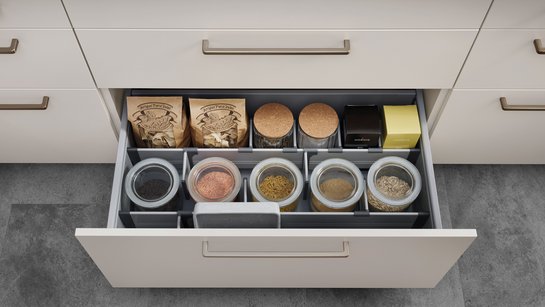 Offene Küchenschublade, darin ein mit Teilern eingeteiltes Ordnungssystem und Lebensmitteln