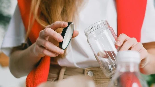 Eine Frau mit einem um die Schultern gehängten orange-farbenen Pullover trennt Glas und Plastik.