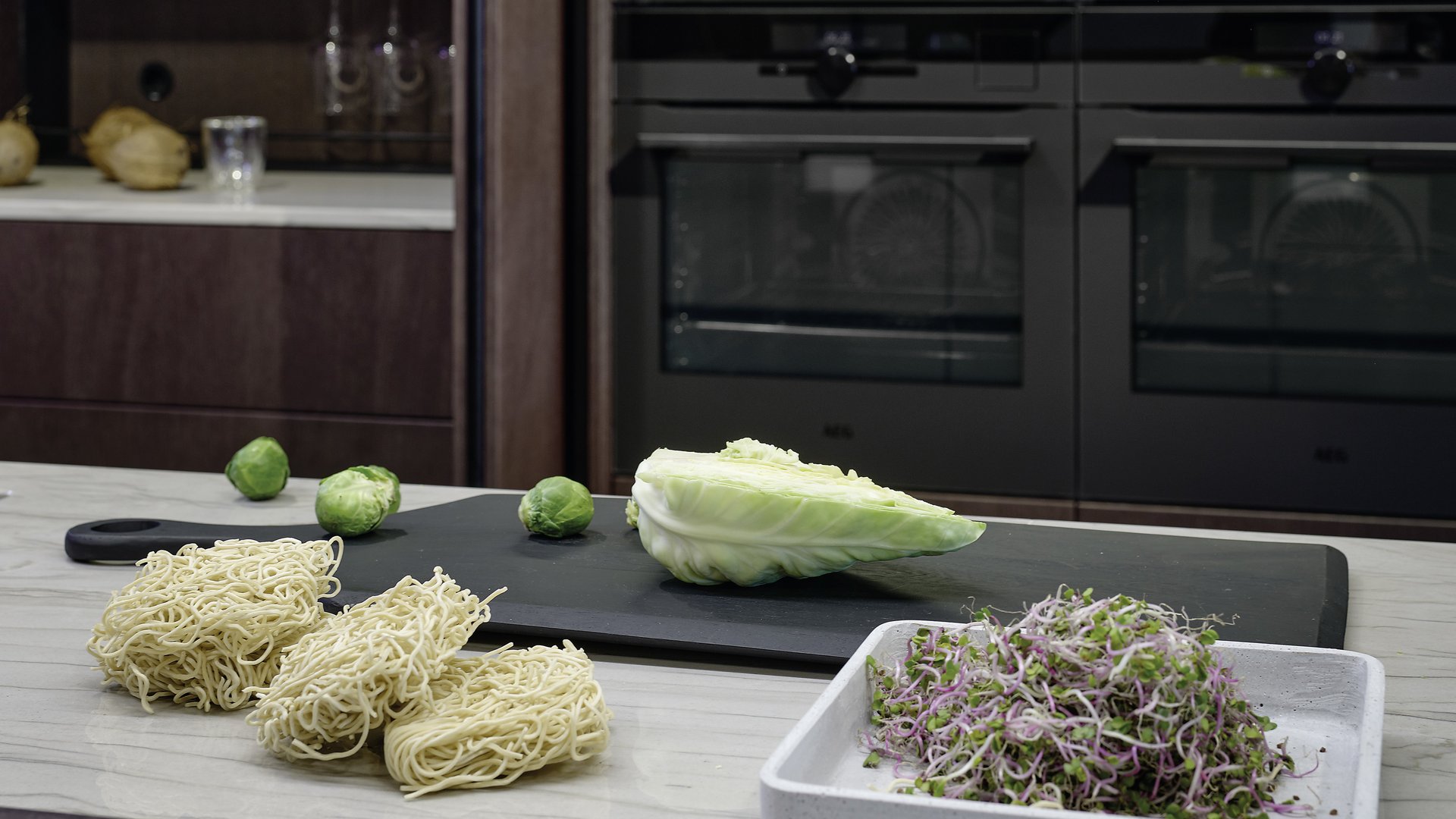 ewe Colora . ewe Nordic in matcha latte . eiche dunkel, Moodbild Microgreens, Salat und getrocknete Nudeln auf einer Küchenarbeitsplatte auf schwarzem Schneidbrett