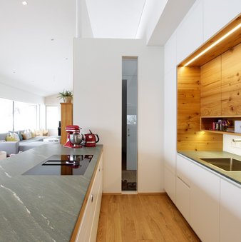 Inselküche in weiß mit grüner Steinarbeitsplatte auf der Kücheninsel, Hochschränke mit Spülnische mit Holz-Oberschränken