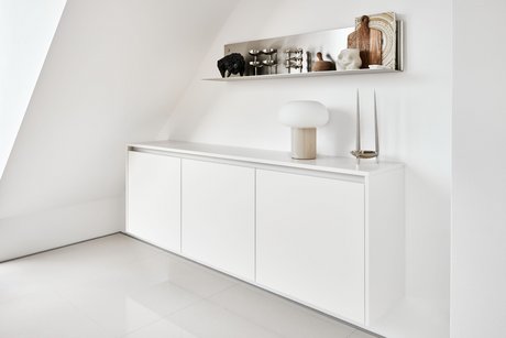 Schwebendes weißes Sideboard an weißer Wand, darüber offene Wandregale