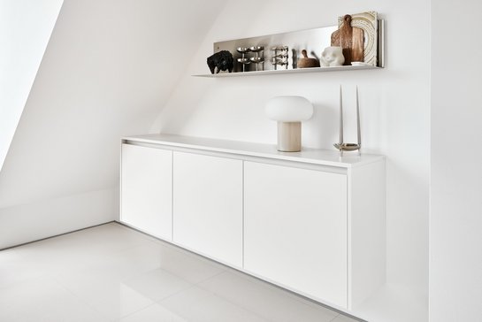 Schwebendes weißes Sideboard an weißer Wand, darüber offene Wandregale