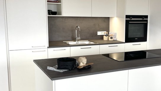 Kompakte kleine weiße Inselküche mit dunkelgrauer Arbeitsplatte und silbernen Griffbügeln