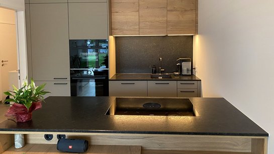 Kompakte Inselküche in lehmbraun mit schwarzer Arbeitsplatte und Oberschränken in Holzoptik