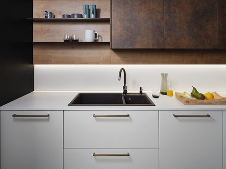 Ausschnitt einer hellen Küchenzeile mit schwarzer Spüle und Armatur, darüber Wandboards, daneben Oberschränke in patina bronze.