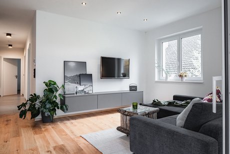 Schlichtes Wohnzimmer mit grauer Couch und einem grauen Sideboard mit Fernseher darüber