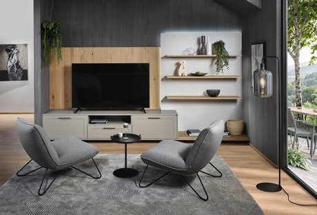 Wohnzimmer mit grauen Fauteuils, grauem Sideboard und hölzerner Wandverkleidung und Wandboarden