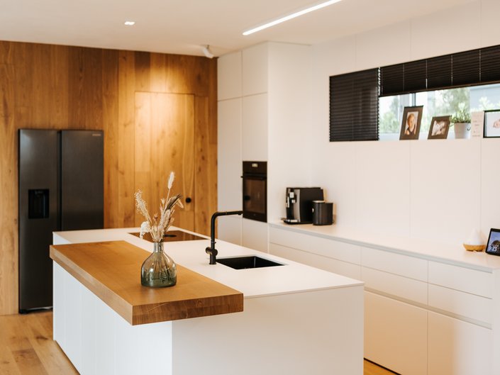 Weiße Inselküche mit Holz-Barplatte auf der Kücheninsel und Hochschränken mit Holzfront.