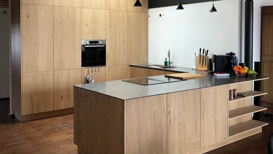 Inselküche mit hellen Holzfronten und deckenhoch verbauten Hochschränken