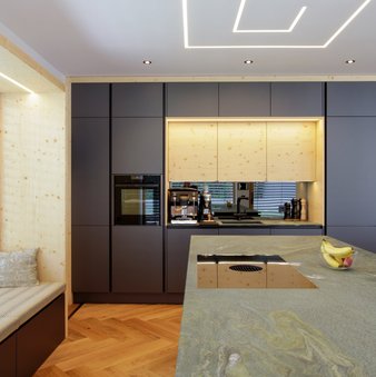 Im Vordergrund eine Kücheninsel mit Arbeitsplatte aus Stein, dahinter eine Küchenzeile in dunkelgrau mit großer holzverkleideter Nische