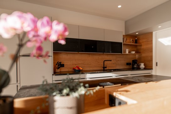 Helle Küche mit Holzoptik-Rückwand, im Vordergrund eine rosa Orchidee