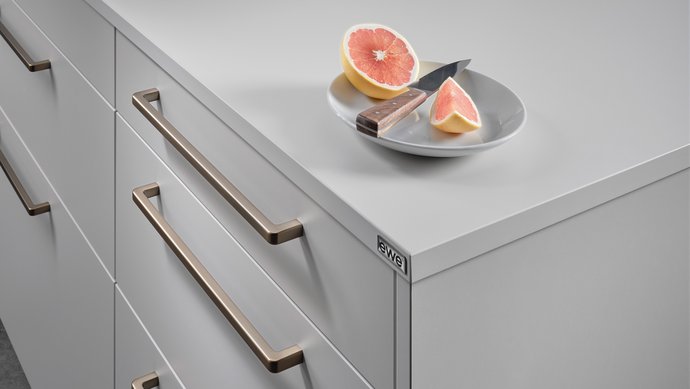 Ausschnitt einer hellgrauen Kücheninsel mit bronzefarbenen Griffbügeln, darauf ein Teller mit Grapefruit