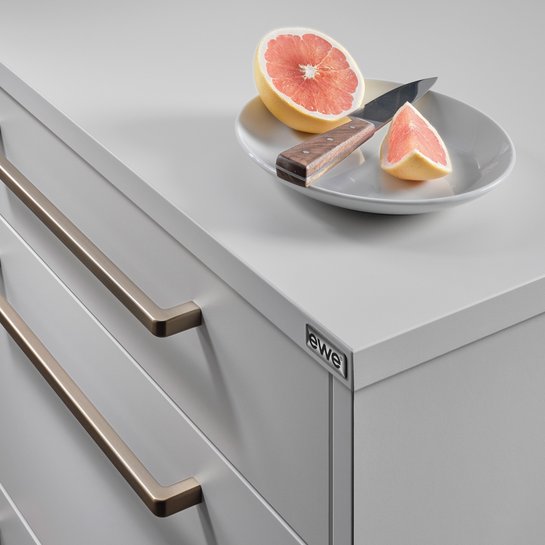 Ausschnitt einer hellgrauen Kücheninsel mit bronzefarbenen Griffbügeln, darauf ein Teller mit Grapefruit