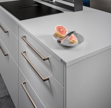 Ausschnitt einer hellgrauen Kücheninsel mit bronzefarbenen Griffbügeln, darauf ein Teller mit Grapefruit