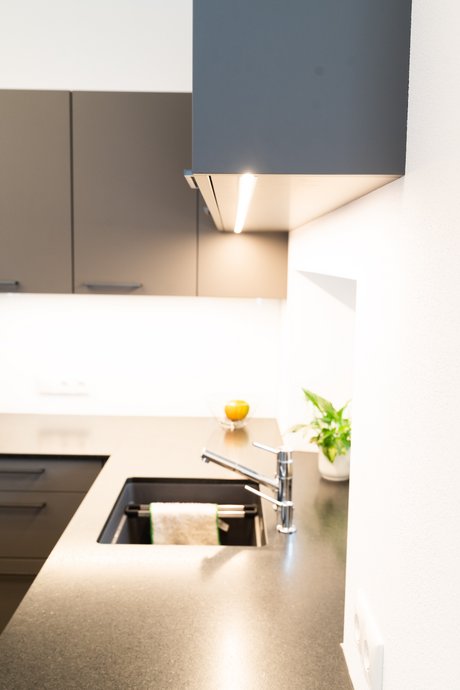 Küchen-Oberschränke in grau mit LED-Beleuchtung über einer Arbeitsplatte mit Spüle