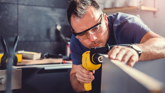 Ein Mann hat einen Bohrer in der Hand und montiert eine Küche