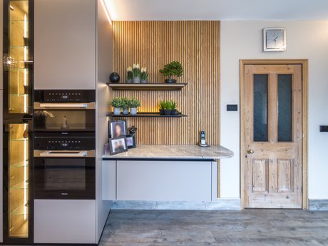 Sideboardlösung mit Holzlamellenwand und beleuchteten Regalen im Wohnbereich.