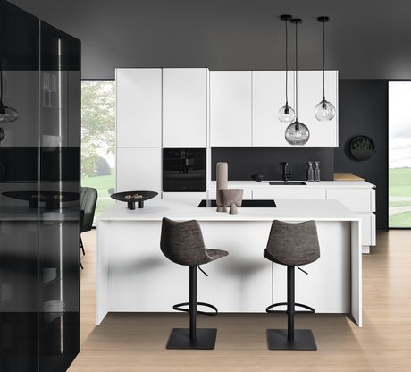 Frontalansicht einer Inselküche in weiß mit dunklen Barstühlen und einem Glasschrank auf der rechten Seite
