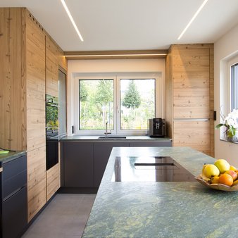 Inselküche mit Arbeitsplatte aus grünem Stein, Küchenfronten in dunkelgrau und kiefer
