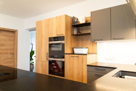 Küche in Holzoptik mit Elektrogeräten, im Vordergrund eine schwarze Arbeitsplatte der Kücheninsel