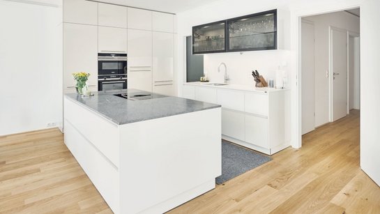 Weiße Inselküche mit grauer Arbeitsplatte aus Stein und Oberschränken mit Glasfronten und schwarzen Rahmen