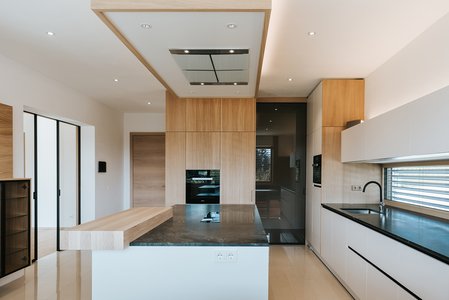 Weiße Küche mit dunkler Arbeitsplatte, aufgesetzter Barplatte aus Holz und Hochschränken aus Eiche