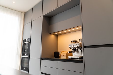 ewe Küche in felsgrau, die durch ihre grifflose Gestaltung und die integrierte beleuchtete Nischenrückwand besticht