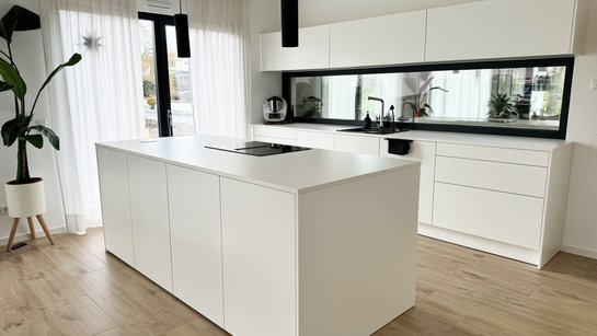 Weiße Inselküche mit weißer Arbeitsplatte in hellem Raum