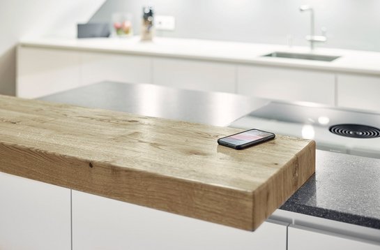 Detailbild einer Barplatte aus Holz auf einer Kücheninsel, auf der ein Smartphone liegt