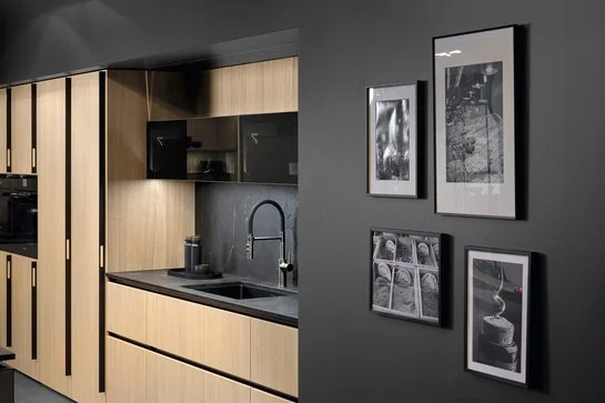Küchenzeile aus hellem Holz umgeben von schwarz gestrichenen Wänden mit Bildern