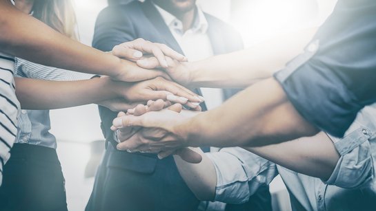 Eine Gruppe Leute hat in der Mitte die Hände im Team zusammengelegt